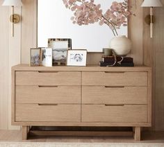 a dresser with flowers and pictures on it in front of a large framed art piece