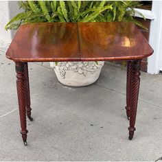 a wooden table sitting on top of a sidewalk next to a potted green plant