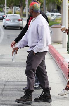 a man walking down the street while holding onto a water bottle and wearing a colorful hat