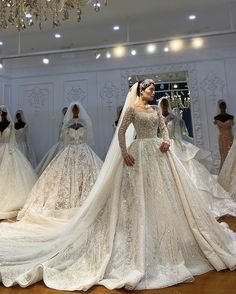 a woman in a wedding dress looking at dresses on mannequins and chandeliers