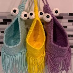 three crocheted purses with googly eyes and fringed handles hanging on a wall