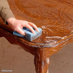 a hand with a sponge on top of a wooden bench that has been stained brown