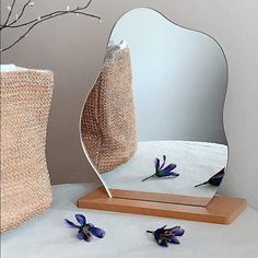 a mirror sitting on top of a white table next to flowers and a vase with purple flowers in it