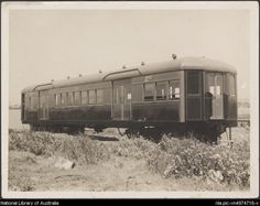 an old black and white photo of a train car on the tracks with weeds in front of it