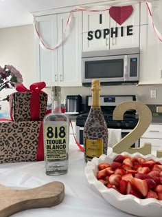 strawberries are in a bowl next to a bottle of booze and two wrapped presents