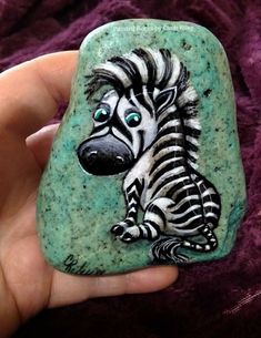 a hand holding a rock with a zebra painted on it's face and eyes