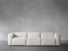 a white couch sitting on top of a cement floor next to a gray wall in an empty room