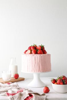 a pink cake with fresh strawberries on top, next to a bowl of strawberries