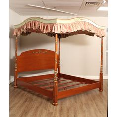 a bed with a pink canopy and wooden frame on the floor next to a white wall