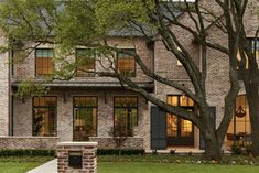 a large brick house with lots of windows and trees in the front yard, surrounded by grass