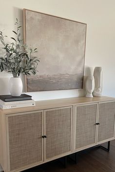 a white vase sitting on top of a wooden cabinet next to a painting and books