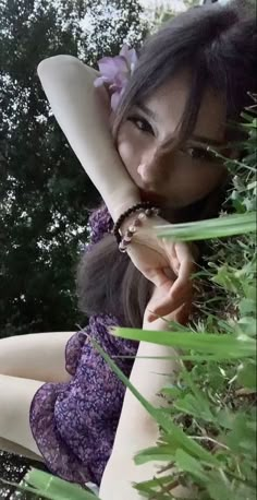 a woman in a purple dress leaning on a tree branch with her hands behind her head