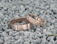 two wedding rings are sitting on the ground next to each other, one has an intricate design