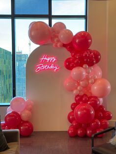 balloon arch with happy birthday sign and balloons in front of large window overlooking cityscape