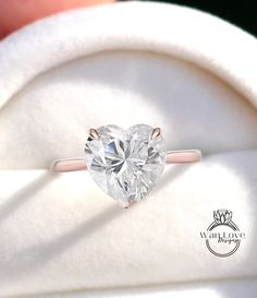 a heart - shaped diamond sits in the middle of a ring that is being held by someone's hand