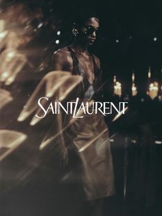 a man standing in front of a dark background with the words saint laurent on it