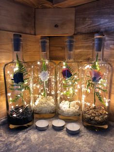 four glass bottles filled with plants and rocks on top of a table covered in lights