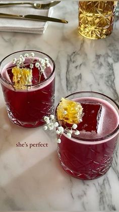 two glasses filled with red liquid and garnished with flowers on the rims