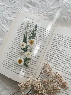 an open book with flowers on top of it next to a flower vase filled with baby's breath