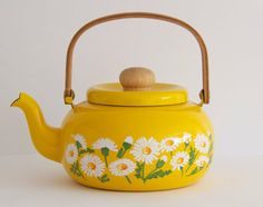 a yellow teapot with daisies painted on it's side and a wooden handle