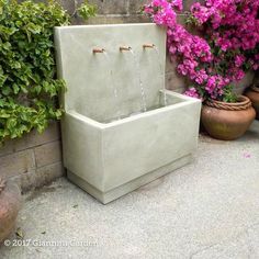 an outdoor fountain with water running from it and some potted plants around the perimeter