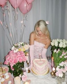 a woman sitting in front of a cake with candles on top of it next to flowers and balloons