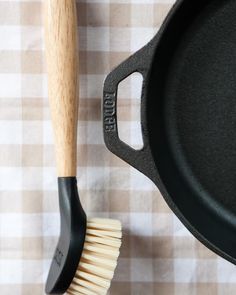 a black pan with a wooden handle next to a white and brown brush on a checkered tablecloth