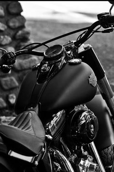 a black and white photo of a motorcycle parked in front of a stone wall,