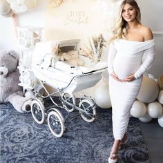 a pregnant woman standing next to a baby carriage in front of balloons and teddy bears