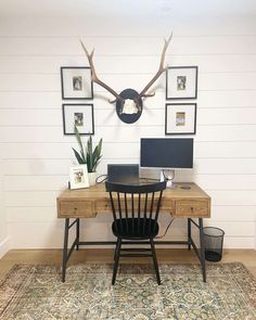 a wooden desk topped with a computer on top of a rug next to a wall mounted deer antlers