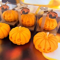 four small pumpkins are sitting in plastic cases on a table with ribbon tied around them