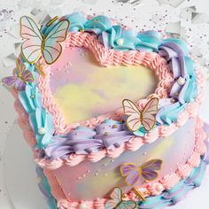 a heart shaped cake with pastel colors and butterflies on the frosting is sitting on a plate