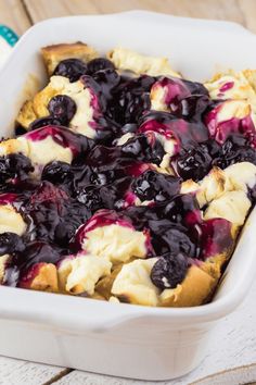 a casserole dish with blueberries and cream in it on a wooden table