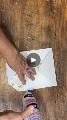 someone is cutting out paper with scissors on a wooden table, while another person holds the edge of an envelope