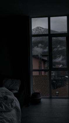 a dark room with a bed, window and mountains outside the window in the background