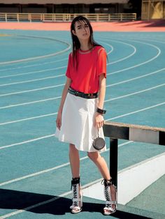 a woman in red shirt and white skirt standing on a track