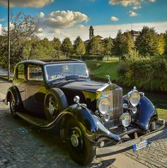 an old fashion car parked on the side of a road in front of a river