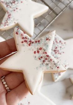 a hand holding a star shaped cookie with sprinkles on it next to other cookies