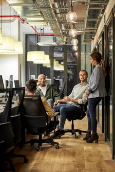 group of people sitting at desks in an office with glass walls and wooden floors