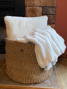 a white blanket is sitting on top of a basket next to a fire place with a fireplace in the background