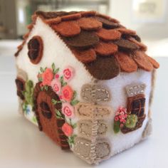 a small house made out of felt with flowers on the roof and windows is sitting on a table