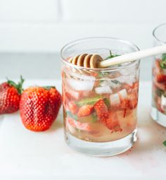 two glasses filled with ice and strawberries on top of a white counter next to some strawberries