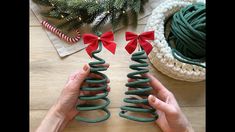 two hands are holding green christmas trees with red bows on them and one hand is pointing at the top