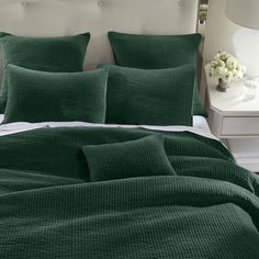 a bed with green comforters and pillows in a white room next to a night stand