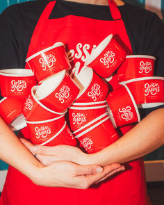 a person in an apron holding a bunch of red cups with white lettering on them