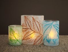 three different colored candles sitting next to each other on top of a cloth covered table