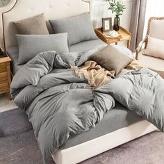 an unmade bed with grey sheets and pillows