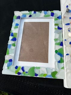 there is a white frame with blue, green and white sea glass on the bottom