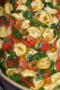 a pot filled with pasta and spinach soup on top of a wooden table next to a spoon