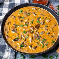 a skillet filled with mushroom soup on top of a checkered table cloth next to bread